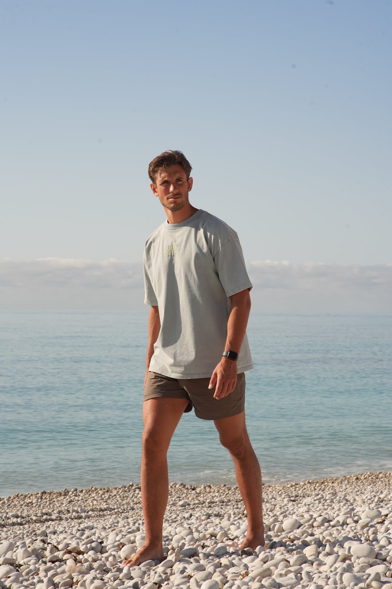 mann som går på en sten strand med en grå blå t skjorte