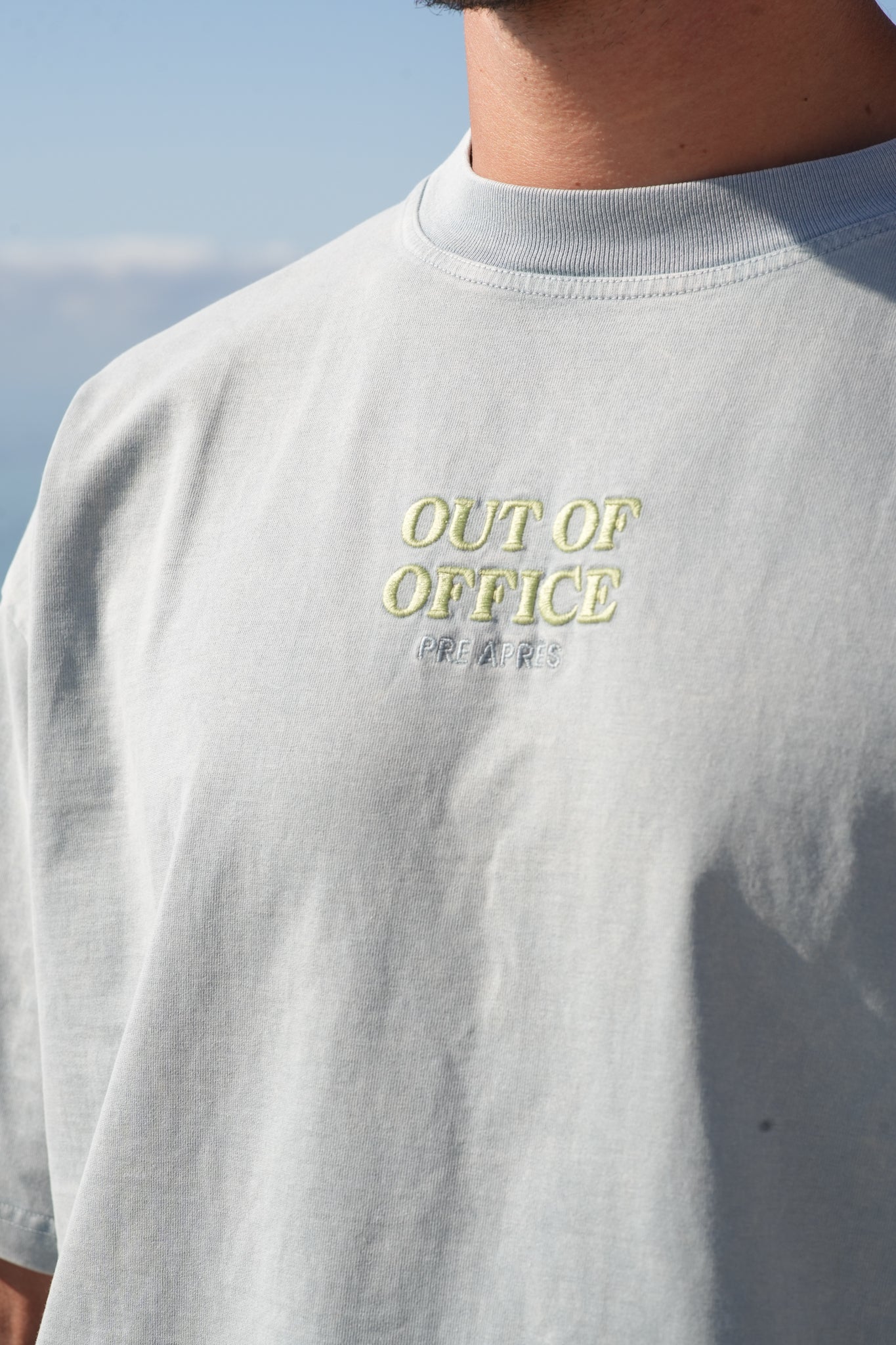 Nærbilde av en lime grønn logo midt på brystet på en grå blå t skjorte