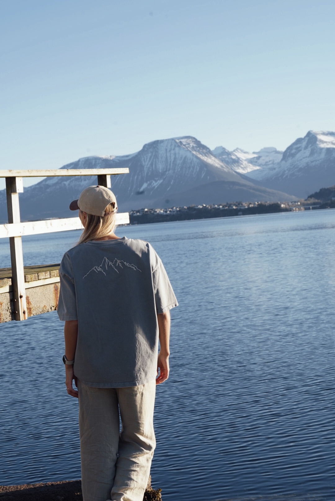 baksiden av en blå t skjorte med hvite streker som illustrerer fjell, og med et vakkert fjellandskap i bakgrunnen